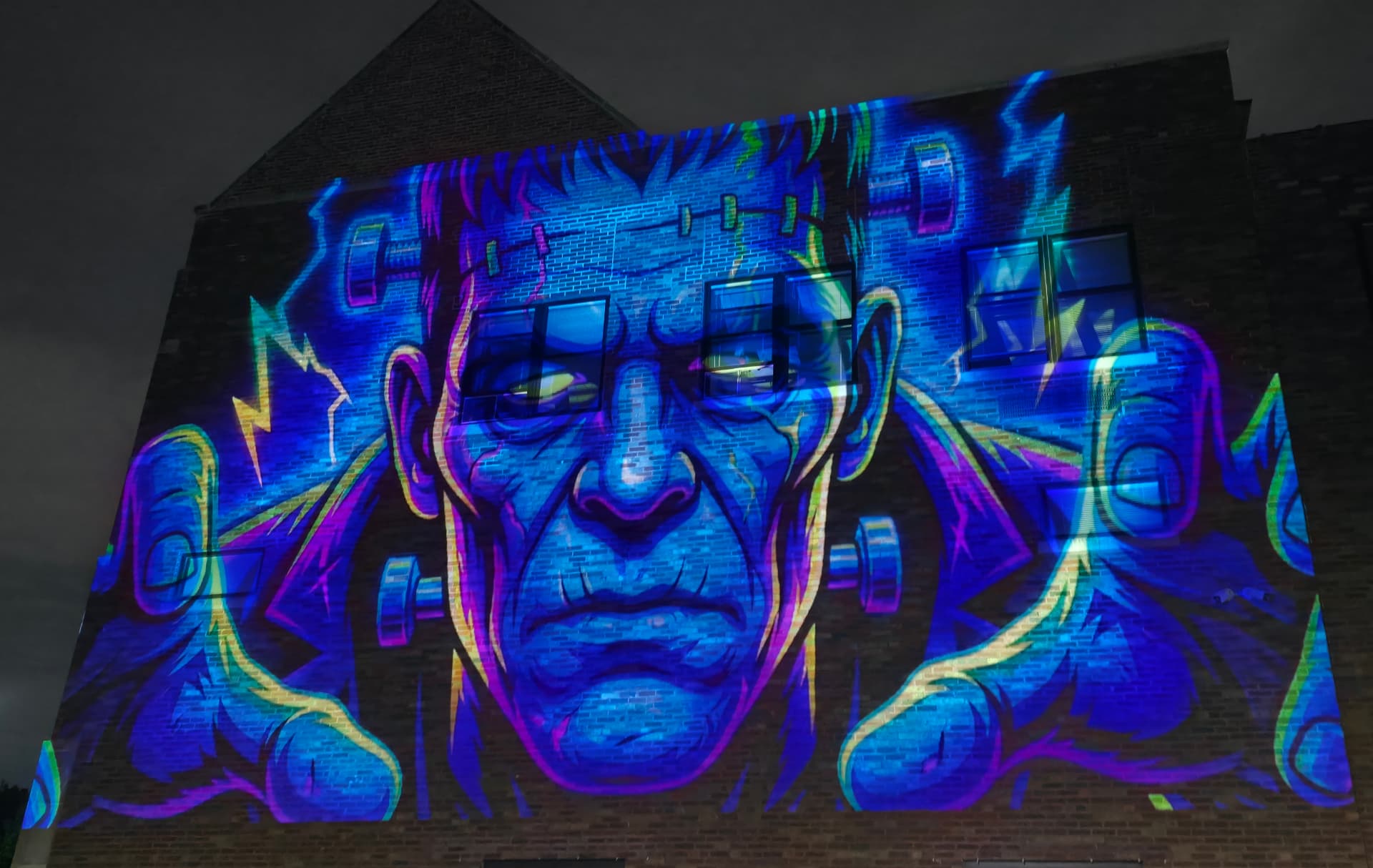 A brick commercial building lit with a giant blue Frankenstein projection