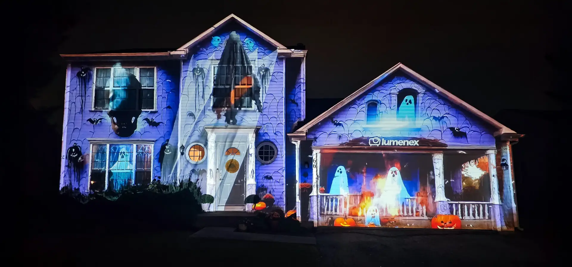 A two-storey house at night with its whole facade projection-mapped in ghosts, bats and cobwebs