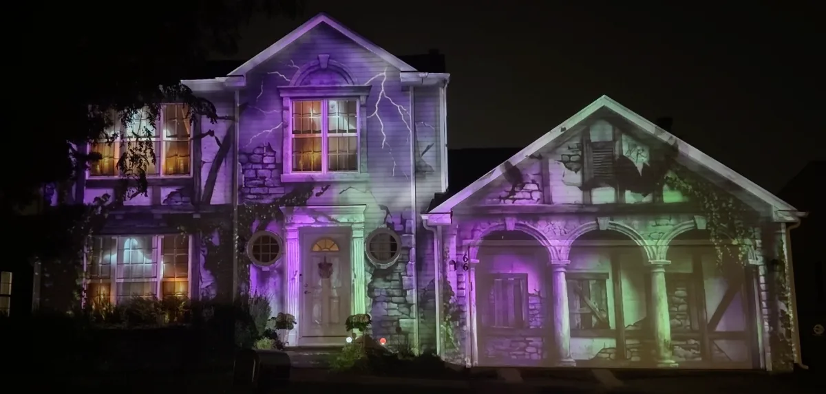 An ordinary house projection-mapped into a crumbling stone mansion, with ivy, lightning and violet and green light